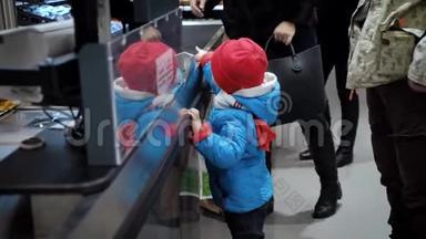 一个3岁的孩子站在超市收银员旁边，看着货物。